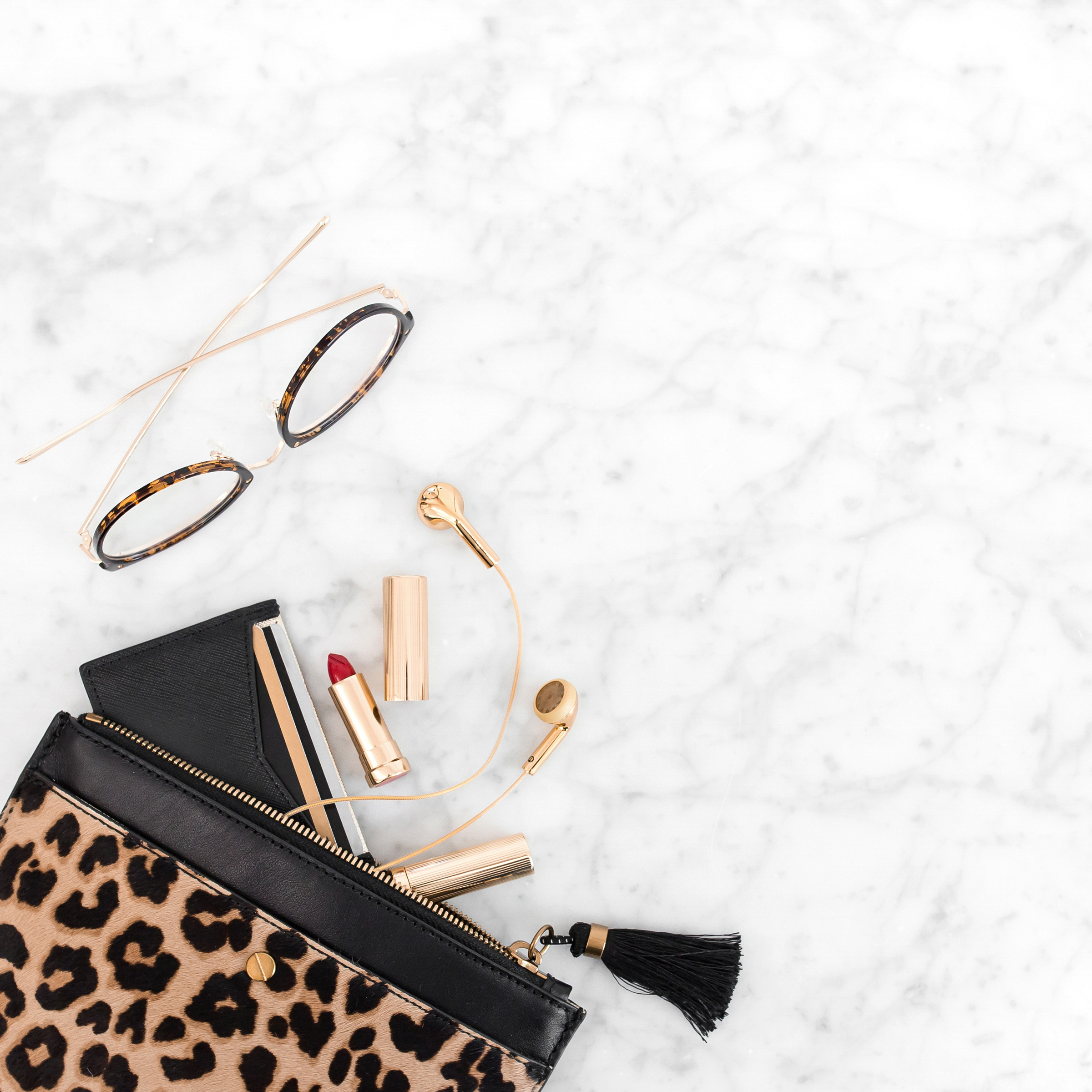 Leopard print clutch with red lipstick, gold earbuds, and tortoiseshell glasses on marble — flat lay representing confidence, self-care, and emotional healing after a breakup.